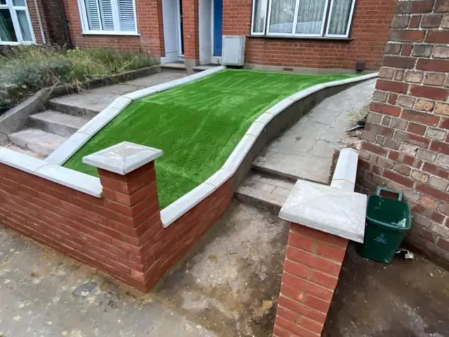 New red brick front garden walls with stone copings, curving beside new steps and a strip of artificial grass in front of a brick terrace