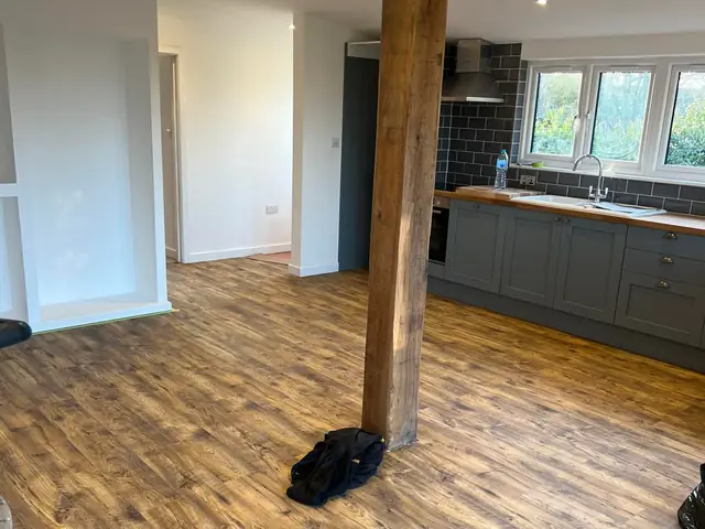 Finished open-plan kitchen and living space with a wood-effect floor, a grey shaker kitchen under the windows and a timber post in the middle of the room