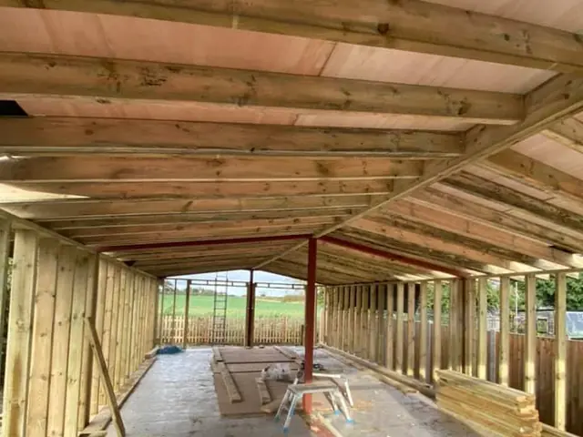 Inside a large new timber-framed building under construction, with roof joists, boarded ceiling and a red steel beam along the floor