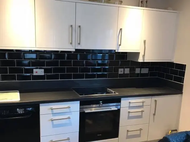 White gloss kitchen with black metro tiles between the wall and base units, a built-in oven and a black worktop